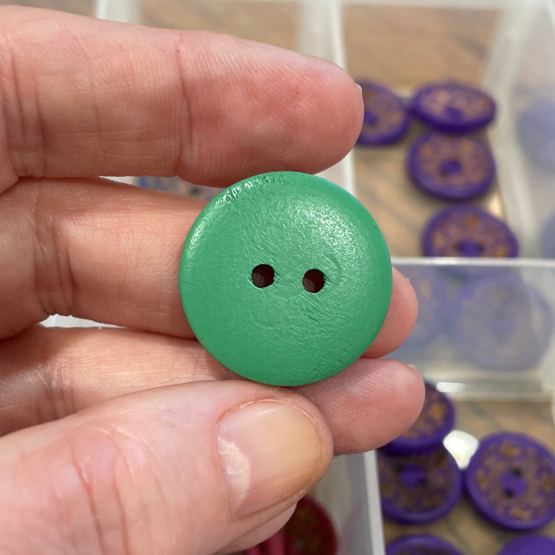 Hand holding a green button with a collection of buttons in a box in the background