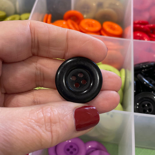 Hand holding a black button with a container of colorful buttons in the background