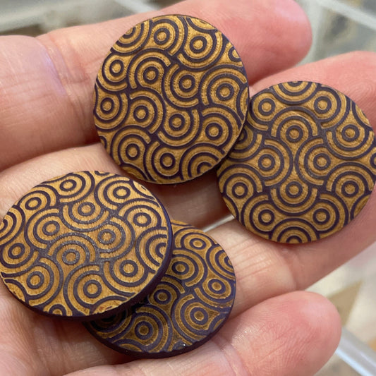 Wooden buttons with intricate patterns held in a hand, with a clear container of similar buttons in the background.