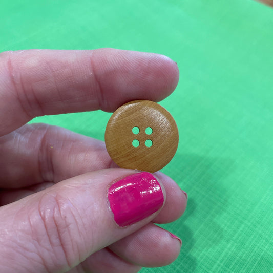 Hand holding a wooden button against a green background