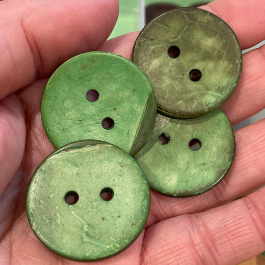 Hand holding four green buttons with a container of gold buttons in the background