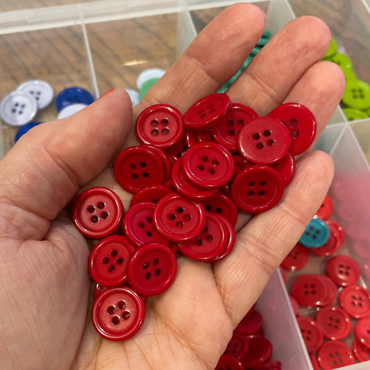 Hand holding red buttons with a container of assorted buttons in the background