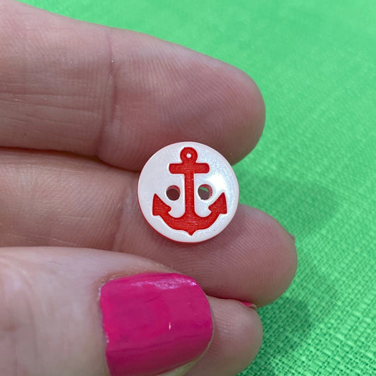 Small round white button with a red design held between fingers against a green background