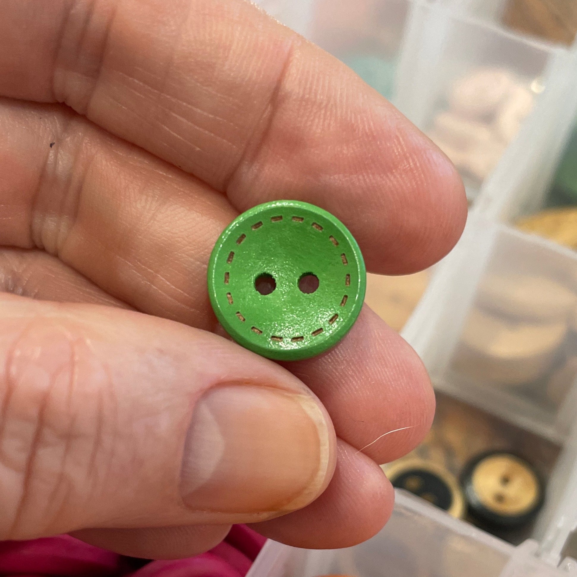 Hand holding a green button with a container of assorted buttons in the background