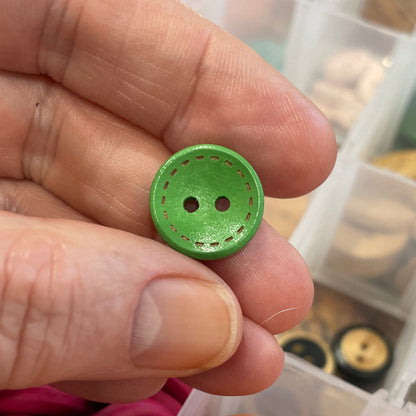 Hand holding a green button with a container of assorted buttons in the background