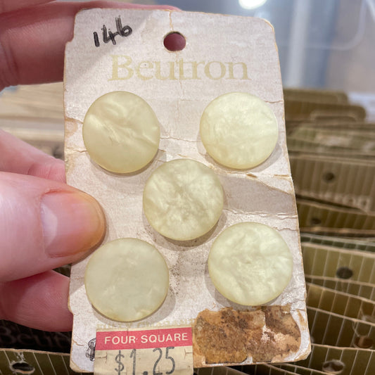 Card with six white buttons held by a hand, with more buttons in the background.