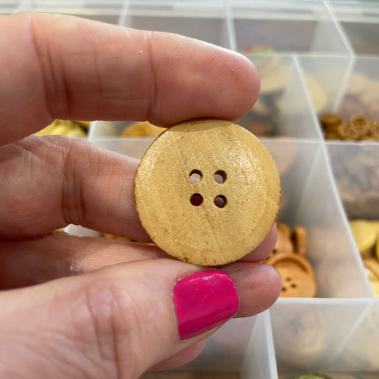 Hand holding a gold button with a collection of buttons in the background