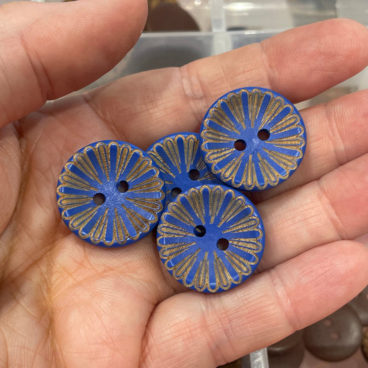 Hand holding blue floral-patterned buttons with a container of assorted buttons in the background.