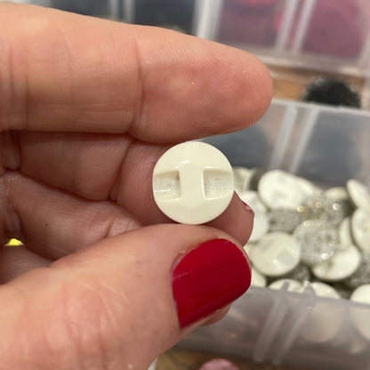 Hand holding a white button with a container of various buttons in the background