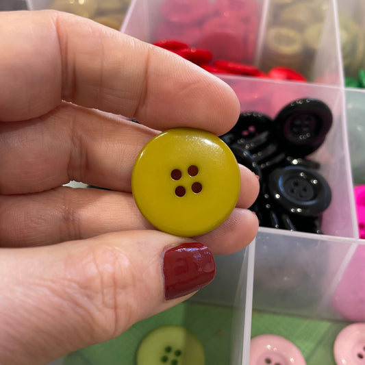 Hand holding a yellow button with a clear container of buttons in the background