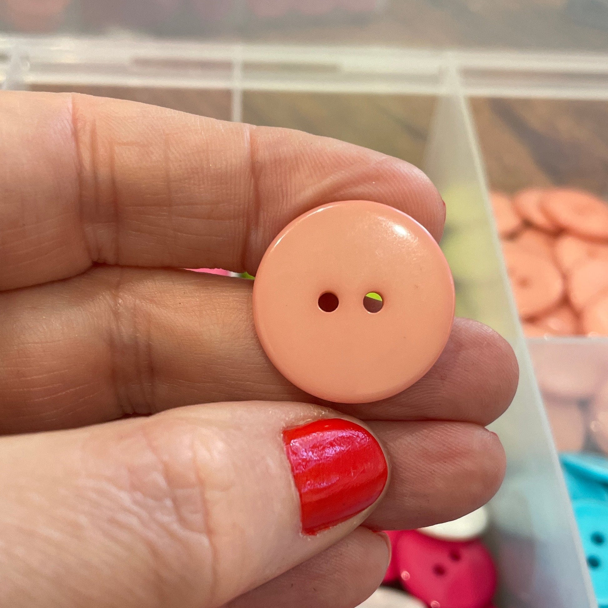 Hand holding a peach-colored button with a container of colorful buttons in the background