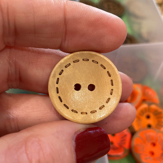 Hand holding a wooden button with a background of colorful buttons