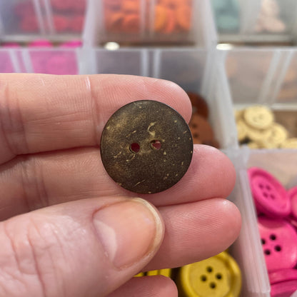 Hand holding a brown button with a container of colorful buttons in the background