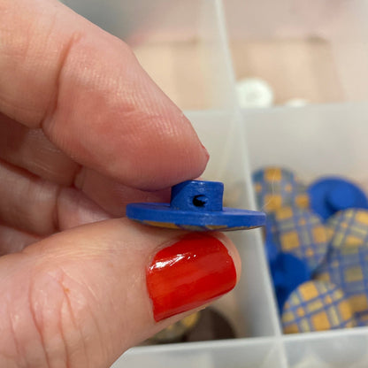 Hand holding a blue button over a container of assorted buttons.