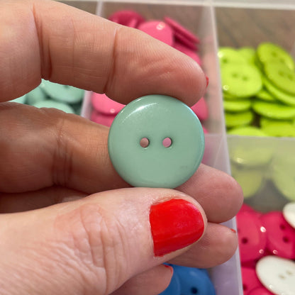 Hand holding a light green button with a colorful button collection in the background