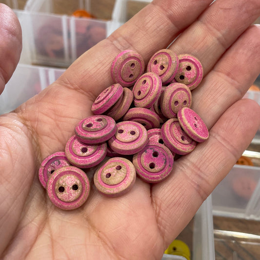 Hand holding pink buttons with a blurred background of a workshop.