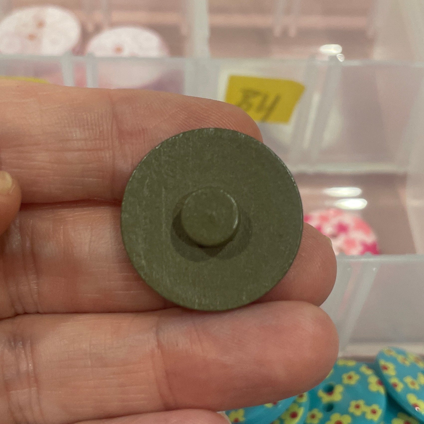Hand holding a green button with a background of various buttons in a container