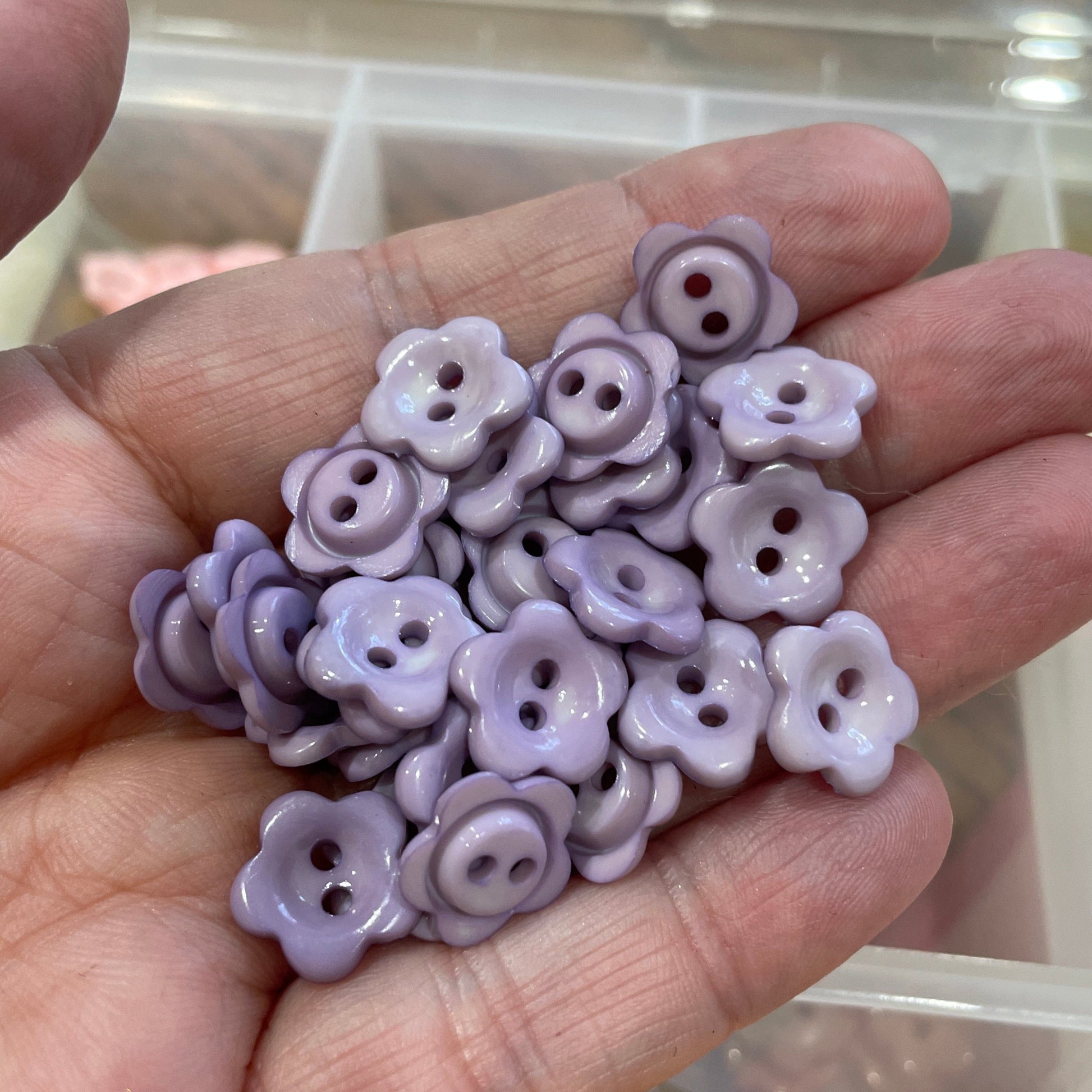 Hand holding purple flower-shaped buttons with a blurred background of more buttons.