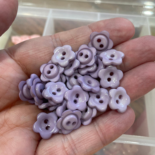 Hand holding purple flower-shaped buttons with a blurred background of more buttons.