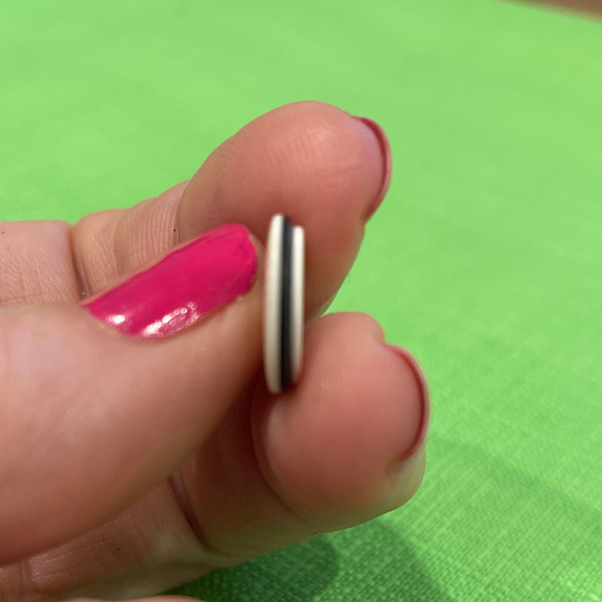 Hand holding a small metallic object against a green fabric background