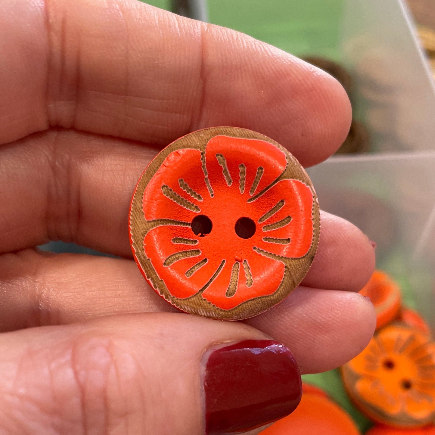 Hand holding an orange button with a decorative edge, surrounded by more buttons in a container.