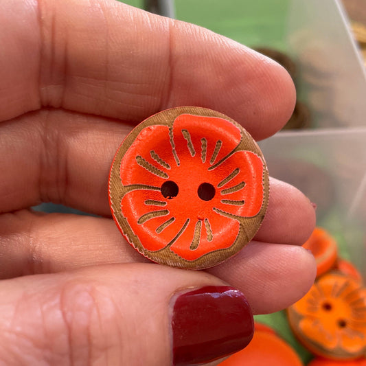 Hand holding an orange button with a decorative edge, surrounded by more buttons in a container.