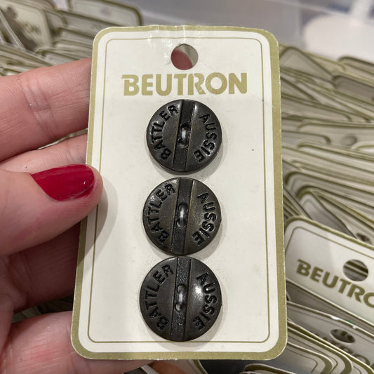 Three buttons labeled 'AUSSIE BATTLER' on a Beutron card held by a hand with red nail polish.