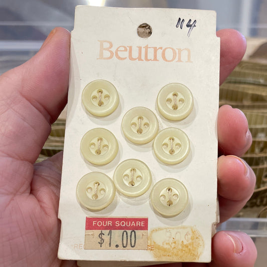 Hand holding a package of buttons with a clear plastic container in the background