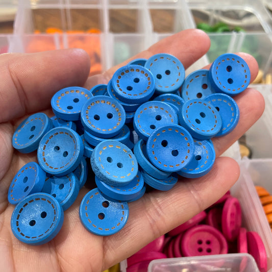 Hand holding blue buttons with a container of assorted buttons in the background