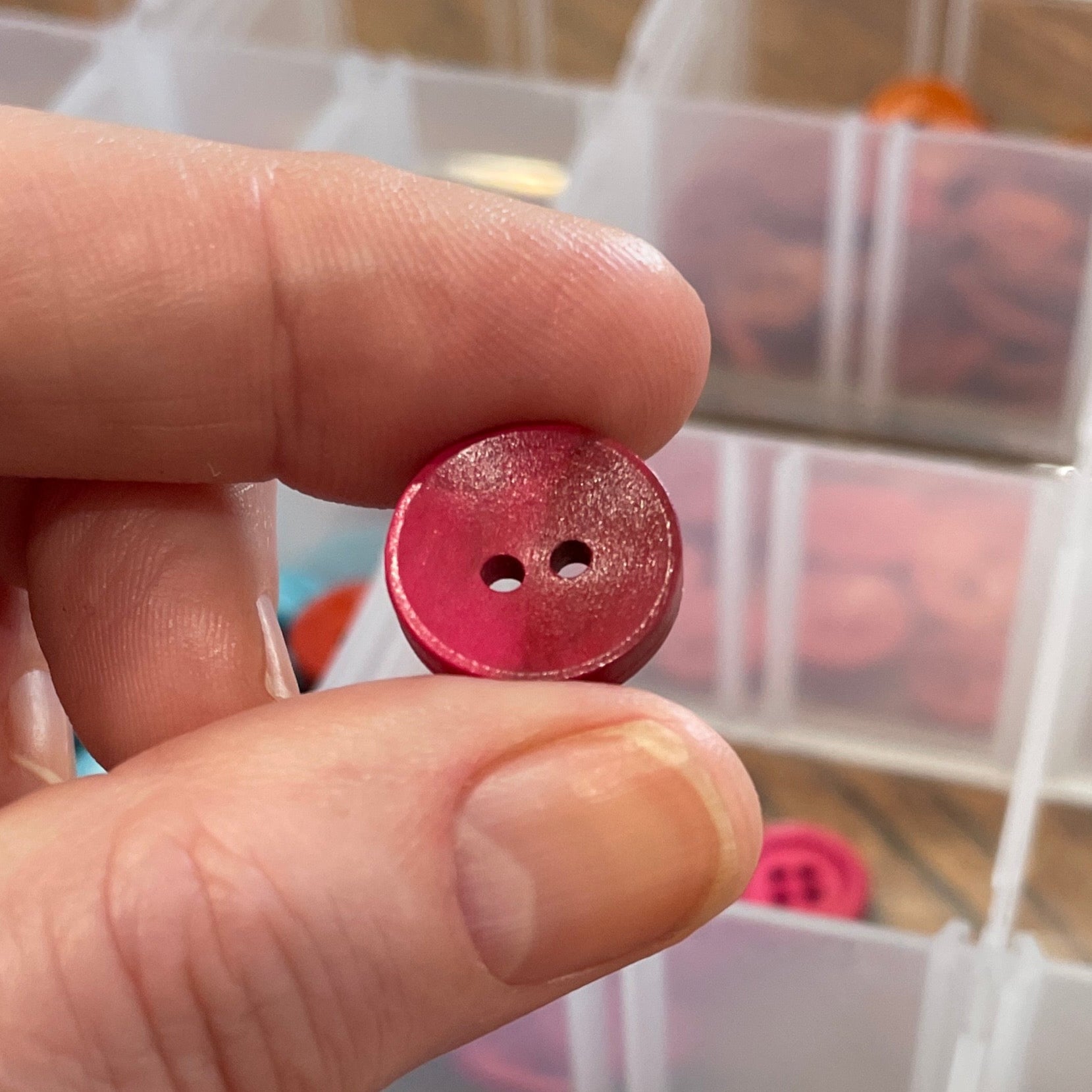 Person holding a pink button with a clear container of buttons in the background