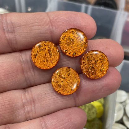 Hand holding orange round stones with containers of various stones in the background
