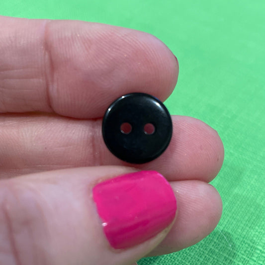 Black button held between fingers with pink nail polish against a green background