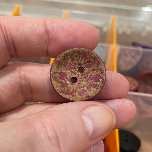 Hand holding a decorative button with a blurred background of a button organizer.