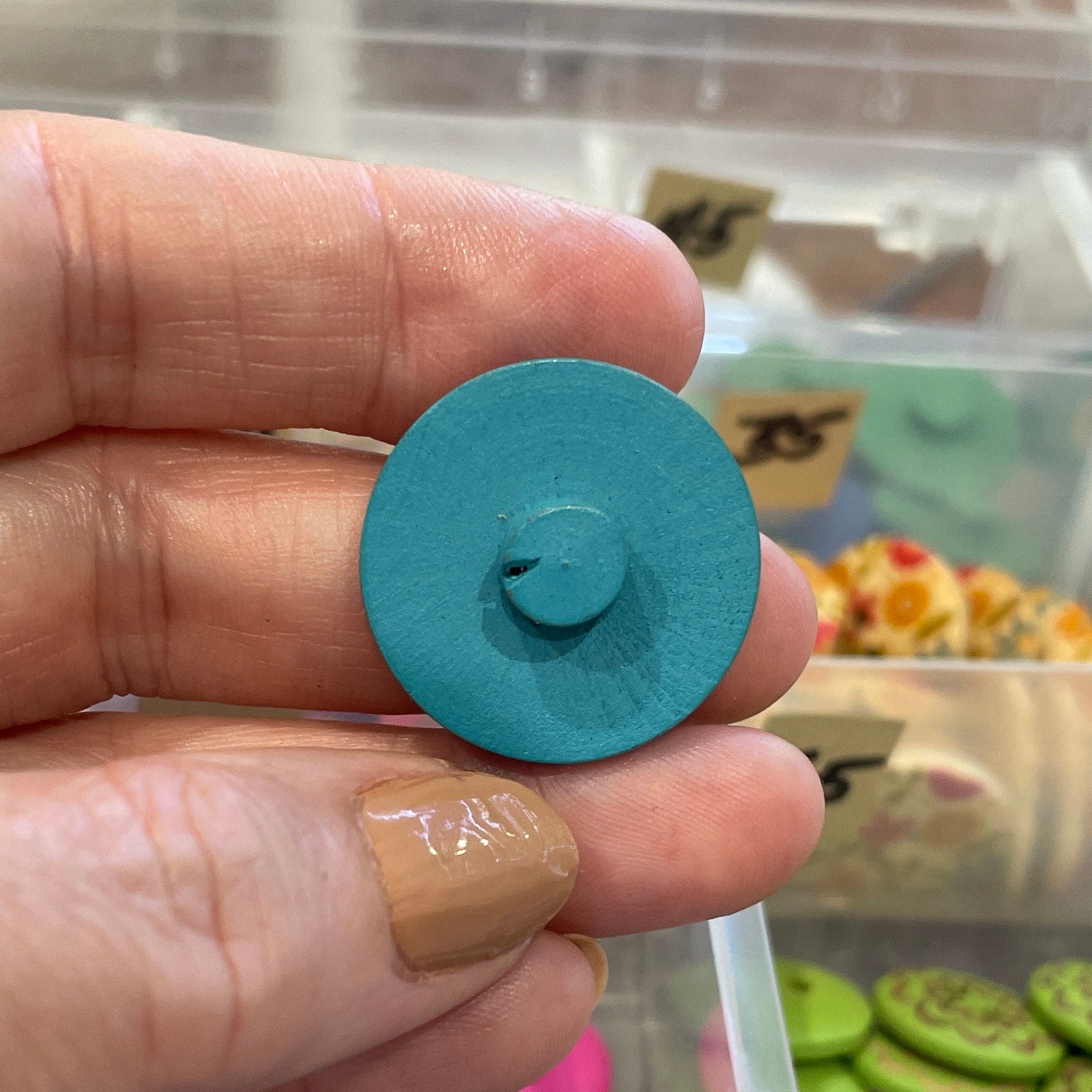 Hand holding a blue button with a container of buttons in the background