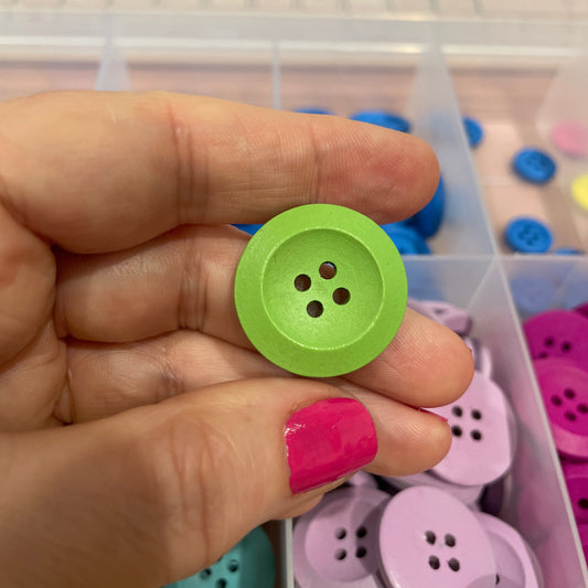 Hand holding a green button with a container of colorful buttons in the background