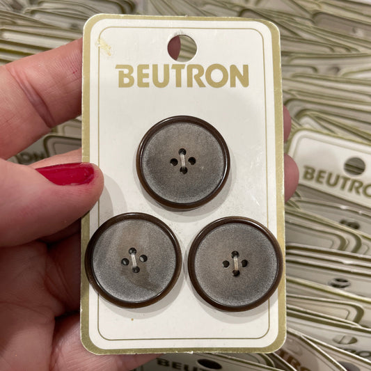 Hand holding a card with three buttons and 'Beutron' branding against a blurred background of similar cards.