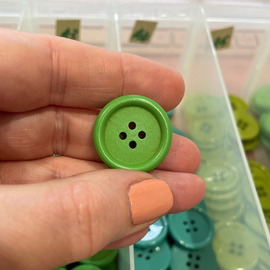 Hand holding a green button with a container of buttons in the background