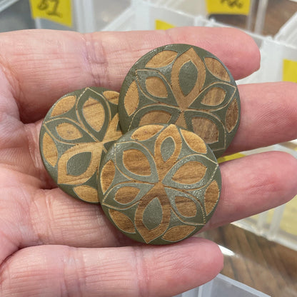 Hand holding two decorative wooden buttons with a button organizer in the background