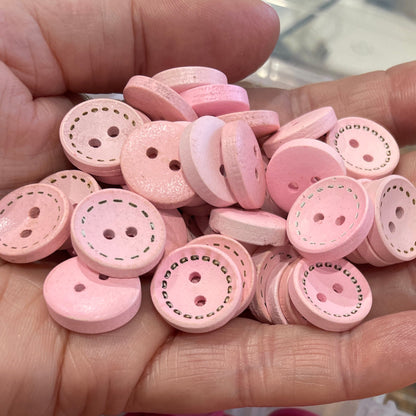 Hand holding pink buttons with a container of orange and pink buttons in the background.