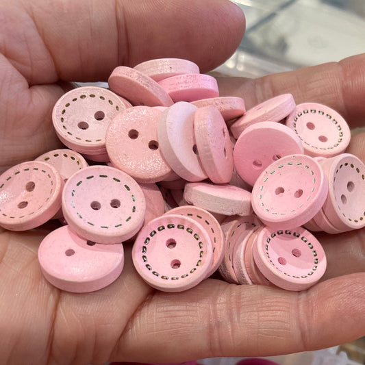 Hand holding pink buttons with a container of orange and pink buttons in the background.