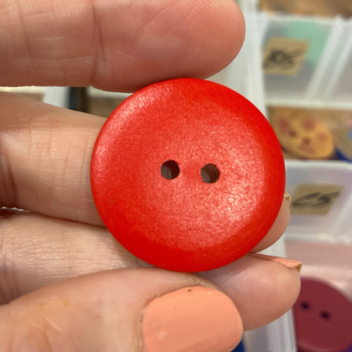 Red button held between fingers with a blurred background of buttons and containers