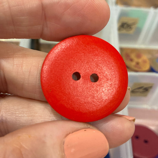 Red button held between fingers with a blurred background of buttons and containers