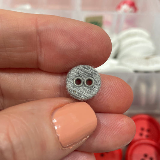 Silver button held between fingers with a container of buttons in the background