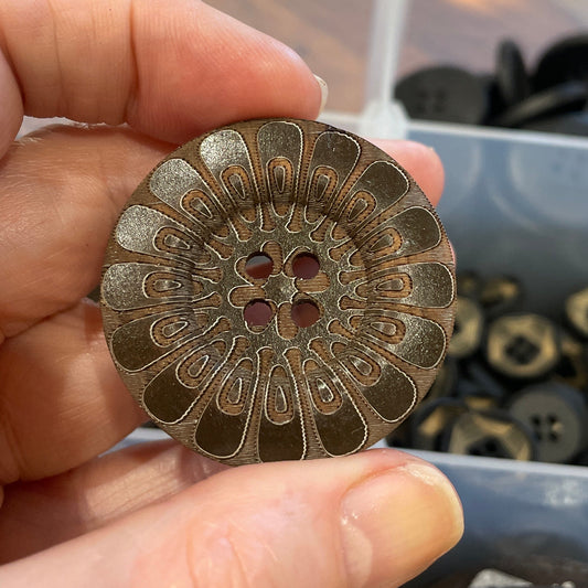 Hand holding a decorative button with intricate design, blurred background of buttons.