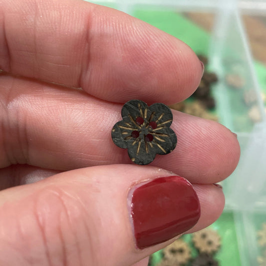 Hand holding a small metal flower-shaped button with a blurred background of buttons.