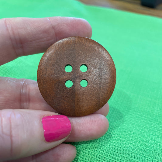 Wooden button held in a hand with pink nail polish against a green fabric background