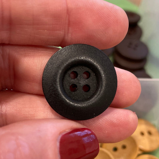 Hand holding a black button with a container of gold buttons in the background