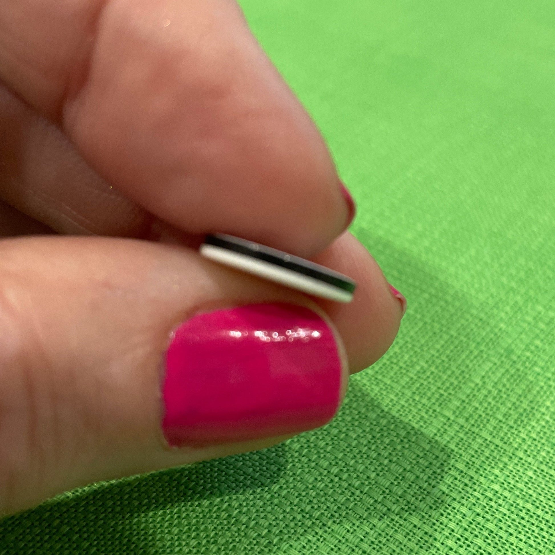 Hand with pink nail polish holding a small object against a green background