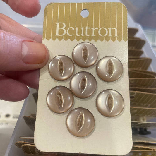 Set of gold buttons on a Beutron card held by a hand with a blurred background