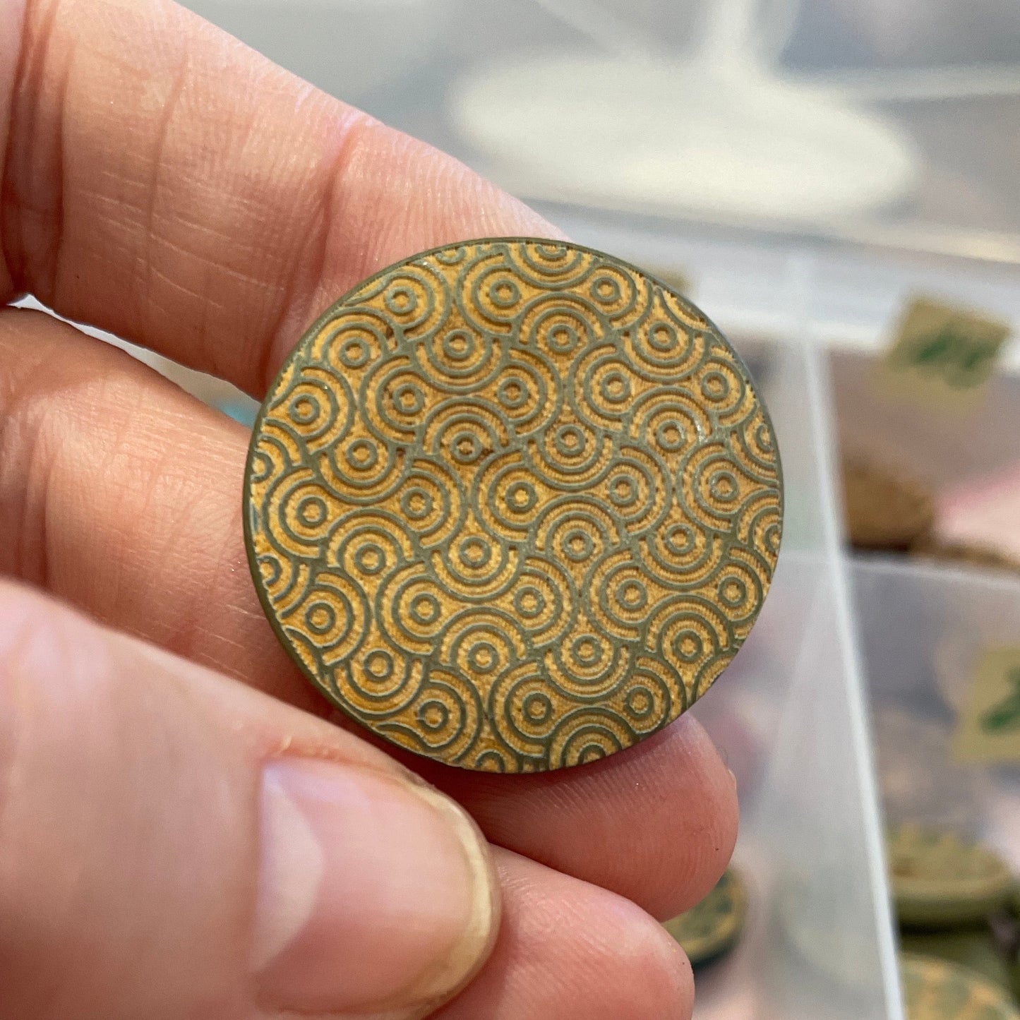 Hand holding a  patterned button with a container of buttons in the background